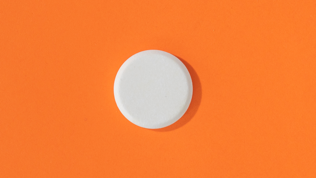 Vitamin D, weiße Tablette vor orangenem Hintergrund